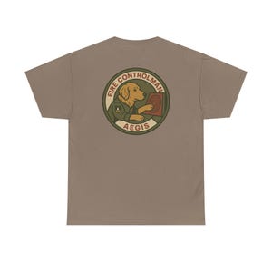May include: A tan t-shirt featuring a circular graphic on the back. The graphic depicts a golden retriever in a military uniform, holding a target, with the words "FIRE CONTROLMAN AEGIS" in a circular design. The shirt is made of a soft material.