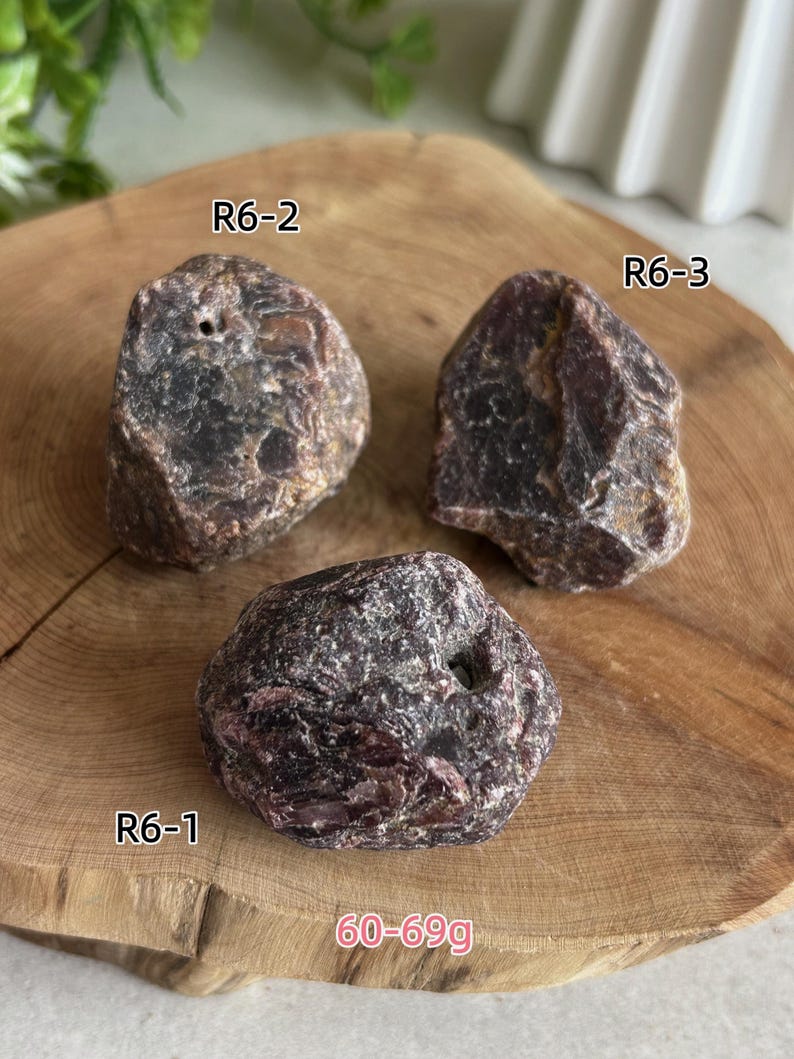Peut inclure: Trois pierres brutes brun-rouge fonc&eacute; aux surfaces irr&eacute;guli&egrave;res et textur&eacute;es. Chaque pierre est &eacute;tiquet&eacute;e avec un code : R6-1, R6-2 et R6-3. Le texte 60-69g est visible en bas, indiquant la plage de poids de ces sp&eacute;cimens min&eacute;raux.