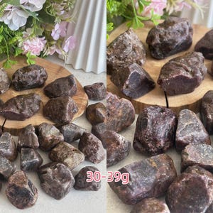 Peut inclure: Une collection de pierres de grenat brutes, brun rouge&acirc;tre fonc&eacute;, aux surfaces irr&eacute;guli&egrave;res et facett&eacute;es. Les pierres varient en taille, certaines pi&egrave;ces &eacute;tant &eacute;tiquet&eacute;es 30-39g. Chaque pierre pr&eacute;sente une teinte terreuse profonde et une texture naturelle brute.
