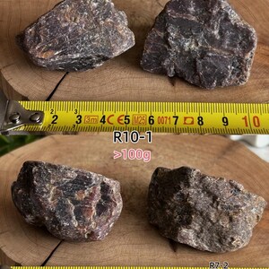 Peut inclure: Deux pierres min&eacute;rales brun fonc&eacute; &agrave; la texture rugueuse sont plac&eacute;es au-dessus d'un m&egrave;tre ruban jaune indiquant une longueur d'environ 10 cm. En dessous, deux autres pierres brun fonc&eacute; sont pr&eacute;sent&eacute;es avec un m&egrave;tre ruban jaune indiquant un poids sup&eacute;rieur &agrave; 100g, &eacute;tiquet&eacute;es R10-1 et R7-2.