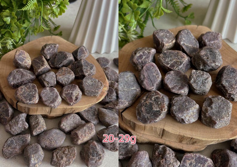 Peut inclure: Une collection de pierres de grenat brutes, brun rouge&acirc;tre fonc&eacute;, aux formes irr&eacute;guli&egrave;res et facett&eacute;es. Les pierres sont &eacute;parpill&eacute;es sur une surface en bois clair, avec une plage de poids de 20-29g imprim&eacute;e en texte rose sur l'image.