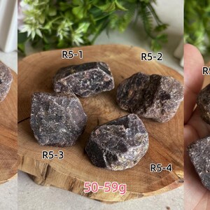 Peut inclure: Quatre pierres min&eacute;rales brutes, brun fonc&eacute;, de forme irr&eacute;guli&egrave;re, &eacute;tiquet&eacute;es R5-1, R5-2, R5-3 et R5-4. Les pierres ont une surface textur&eacute;e et cristalline et sont pr&eacute;sent&eacute;es en groupe, avec un poids total indiqu&eacute; de 50-59g sur l'image.