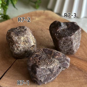 Peut inclure: Trois pierres brutes brun fonc&eacute; aux surfaces textur&eacute;es, &eacute;tiquet&eacute;es R7-1, R7-2 et R7-3. Les pierres sont regroup&eacute;es et le texte 70-79g est visible, indiquant leur poids en grammes. Chaque pierre pr&eacute;sente une forme irr&eacute;guli&egrave;re unique.