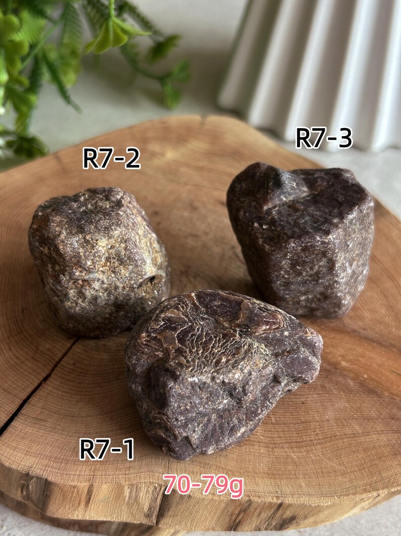 Peut inclure: Trois pierres brutes brun fonc&eacute; aux surfaces textur&eacute;es, &eacute;tiquet&eacute;es R7-1, R7-2 et R7-3. Les pierres sont regroup&eacute;es et le texte 70-79g est visible, indiquant leur poids en grammes. Chaque pierre pr&eacute;sente une forme irr&eacute;guli&egrave;re unique.