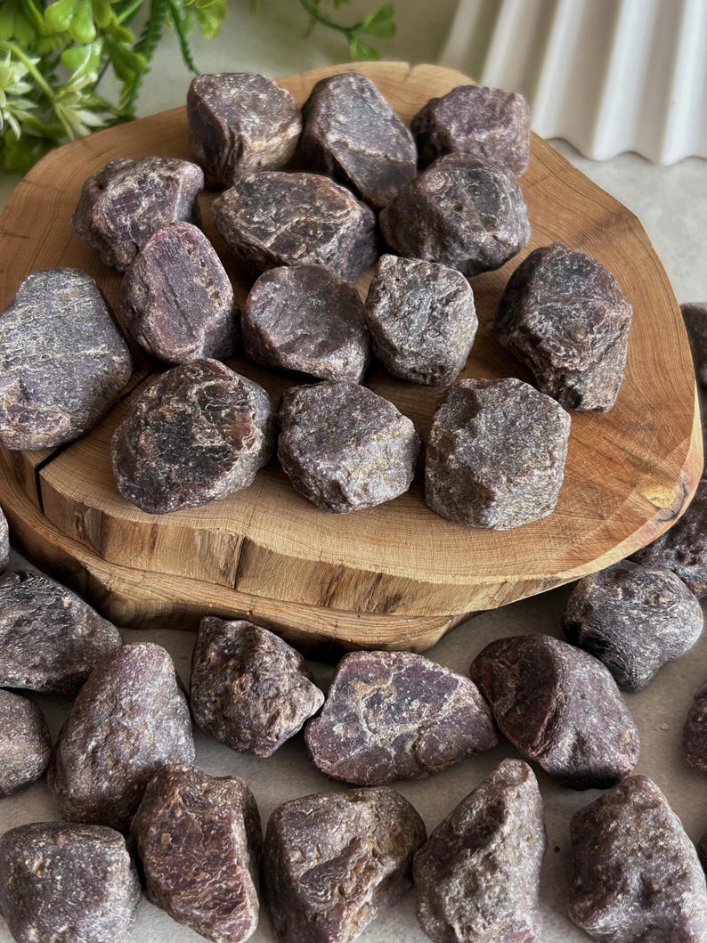 Peut inclure: Une collection de pierres de grenat brutes, non polies, de couleur marron fonc&eacute; et rouge brun&acirc;tre, aux formes irr&eacute;guli&egrave;res et dentel&eacute;es avec des surfaces textur&eacute;es. Ces sp&eacute;cimens min&eacute;raux naturels sont &eacute;parpill&eacute;s sur une tranche de bois.