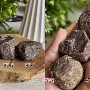 Peut inclure: Trois pierres brutes, brun fonc&eacute;, de forme irr&eacute;guli&egrave;re, &eacute;tiquet&eacute;es R7-1, R7-2 et R7-3. Les pierres ont une surface textur&eacute;e et cristalline et p&egrave;sent entre 70 et 79g. Elles sont pr&eacute;sent&eacute;es sur une tranche de bois et dans une paume.