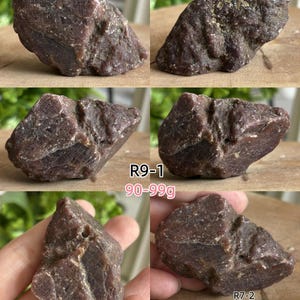Peut inclure: Un sp&eacute;cimen min&eacute;ral brut brun rouge&acirc;tre fonc&eacute; avec une texture cristalline rugueuse et des facettes irr&eacute;guli&egrave;res. La pierre est &eacute;tiquet&eacute;e R9-1 avec un poids de 90-99g et R7-2, montr&eacute;e &agrave; c&ocirc;t&eacute; d'un m&egrave;tre ruban jaune indiquant plus de 5 centim&egrave;tres.