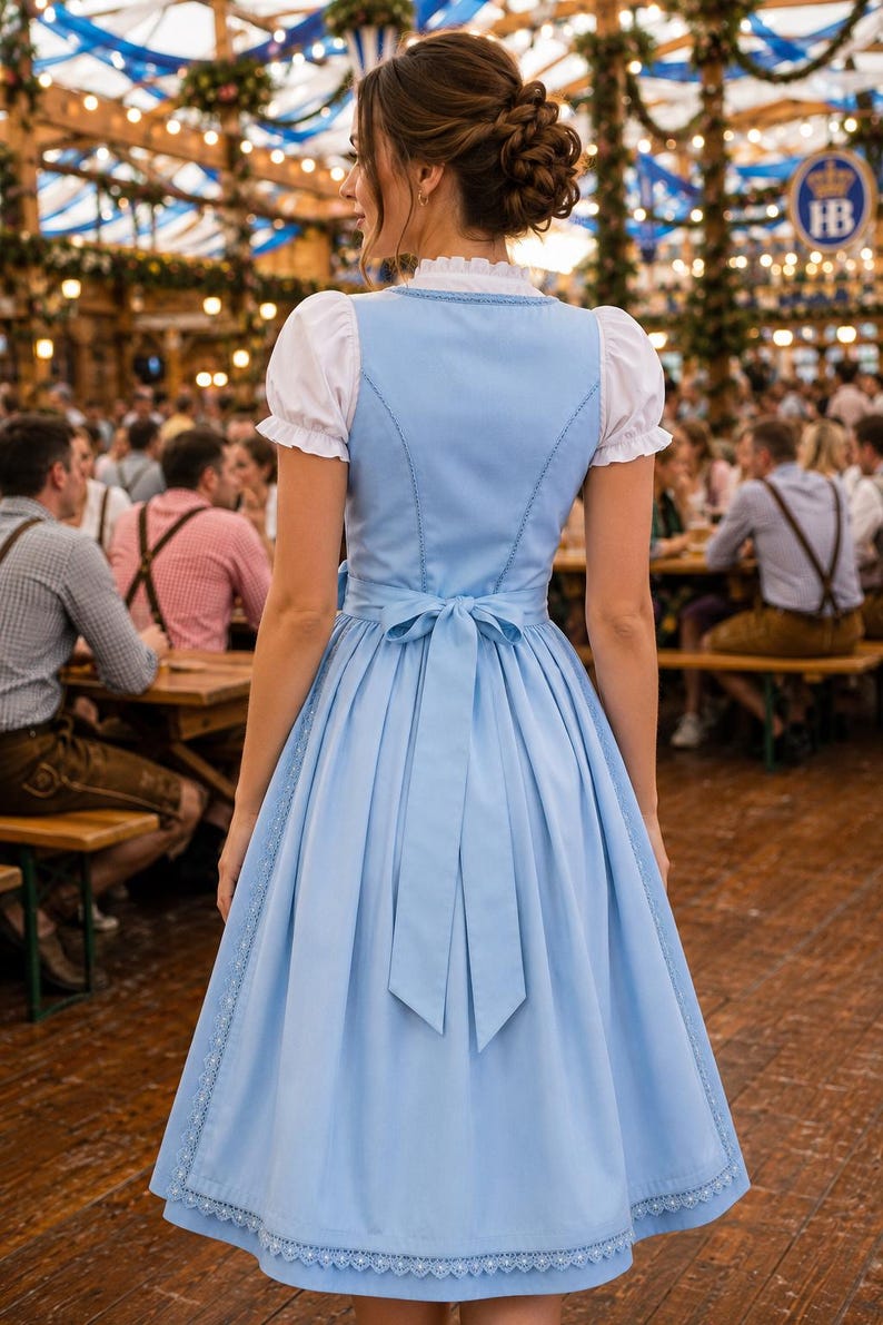 May include: A light blue dirndl dress featuring a white blouse with short puffed sleeves, a high neckline, and a fitted bodice. The skirt is knee-length with a decorative lace trim along the hem and a matching blue fabric tie at the waist.