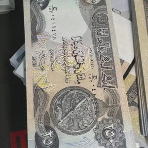 Könnte beinhalten: Ein hellfarbiger 250-Dinar-Geldschein mit aufwendigen Designs und arabischem Text. Die Banknote zeigt ein kreisförmiges Emblem mit einem Kompass und anderen komplizierten Mustern. Die Zahl 250 ist deutlich sichtbar.