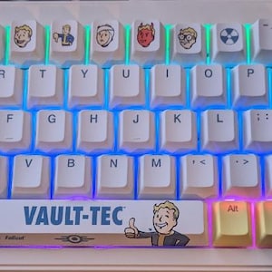 May include: A mechanical keyboard with white and yellow keycaps. The keycaps feature various cartoon character designs and the text "VAULT-TEC". The keyboard has a backlight with blue, purple, and green hues.