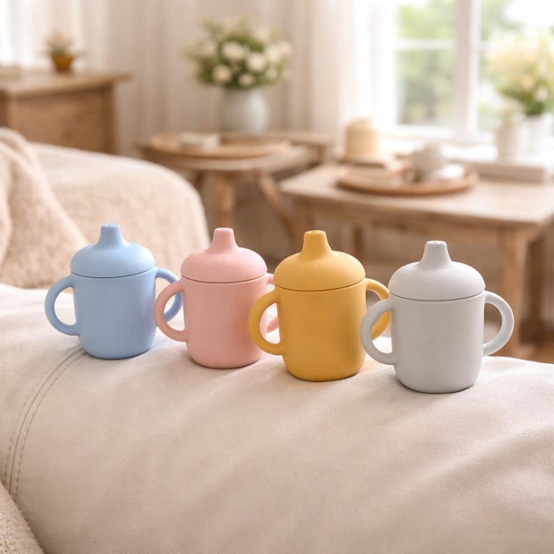 May include: Four pastel-colored baby sippy cups with handles and lids. The cups are light blue, pink, yellow, and white. The cups are made of a soft material and are designed for easy gripping.