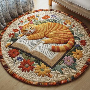 May include: A round, beige rug with an embroidered design. An orange tabby cat is sleeping on an open book, surrounded by colorful embroidered flowers. The rug has a decorative border with orange and brown squares.