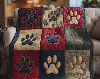 May include: A patchwork quilt featuring large paw prints in various colors. The quilt has a mix of red, tan, and navy blue squares, each with a different paw print design. The quilt is bordered with a dark blue fabric.