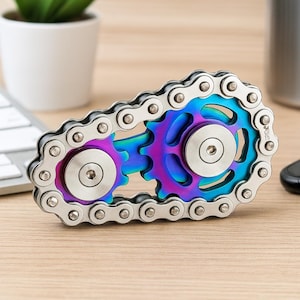 以下が含まれることがあります： 自転車のチェーンとギアの形をした、銀色の金属製フィジェットスピナー。 ギアは紫、青、緑の色合いの虹色の仕上がりです。 スピナーは木製の表面に置かれています。