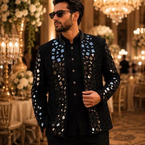 May include: A black jacket with a geometric pattern of mirrored squares, worn over a black shirt and pants. The jacket has a mandarin collar and is paired with black sunglasses. The setting appears to be a formal event.