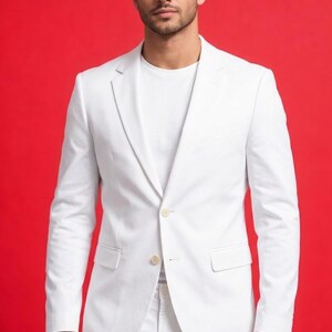 May include: A white suit, consisting of a blazer and pants, is shown against a red background. The blazer has a single-button closure and a notched lapel. The outfit is completed with a white t-shirt.