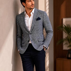 May include: A black and white plaid blazer with a white dress shirt and navy blue pants. The blazer has a classic pattern and a pocket square. A watch is visible on the wrist. The outfit is a stylish ensemble.