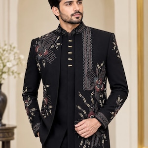 Könnte beinhalten: Eine schwarze Sherwani-Jacke mit hohem Stehkragen und aufwendiger Blumenstickerei in Dunkelrot, Grau und Gold. Die Jacke wird über einem passenden schwarzen Kurta mit goldfarbenen Knöpfen und einer schwarzen Hose getragen.