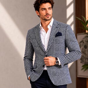 May include: A black and white checkered blazer with a navy blue pocket square. The blazer is worn over a white dress shirt. A brown leather watch is visible on the wrist. The overall look is stylish and sophisticated.