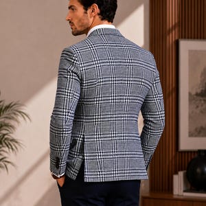 May include: A navy and white plaid blazer with a white dress shirt. The blazer has a classic fit and is paired with navy blue trousers. The man is standing with his hands in his pockets.