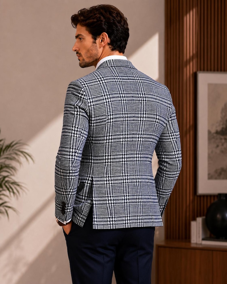 May include: A navy and white plaid blazer with a white dress shirt. The blazer has a classic fit and is paired with navy blue trousers. The man is standing with his hands in his pockets.