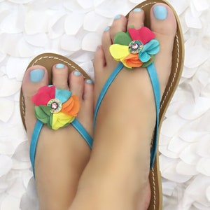 May include: A pair of blue and brown thong sandals with a colorful flower embellishment on each strap.