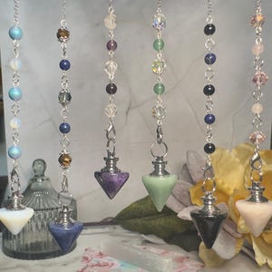 May include: Six hanging pendulums featuring silver-toned chains and various gemstone beads. Each pendulum ends in a pointed, faceted stone pendant in colors including white, blue, purple, light green, black, and pale pink, attached by a metal clasp.