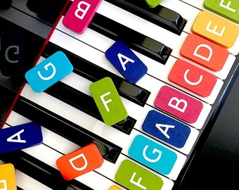 May include: A black and white keyboard with colorful letter tiles on top. The tiles spell out the letters A, B, C, D, E, F, G, and so on. The tiles are in different colors, including red, blue, green, yellow, and orange.