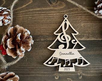 May include: A wooden Christmas tree ornament with a treble clef and musical notes cut out. The ornament is personalized with the name "Samantha" and the year "2023".