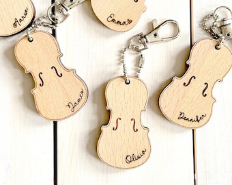 Puede incluir: Cinco llaveros de madera con forma de violín con anillas de plata. Cada llavero está grabado con un nombre diferente: Aaron, Emma, James, Jennifer y Olivia.
