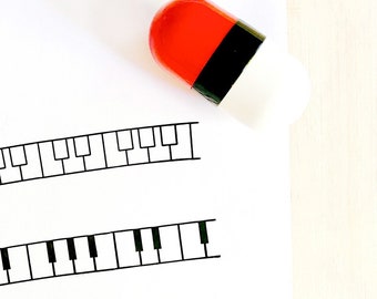 以下が含まれることがあります： 白紙に黒と白のピアノの鍵盤のデザインが2つ描かれています。赤と白の錠剤が紙の上に置かれています。