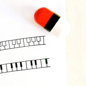 May include: A white sheet of paper with two black and white piano key designs. A red and white pill is on the paper.
