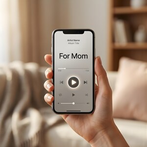 May include: A smartphone displaying a music player interface with the text "For Mom" on the screen. The interface shows a play button, time indicators, and other music control icons. The phone is held in a hand.