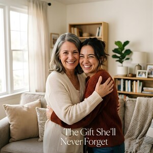 May include: Two smiling women embracing, one with gray hair and a cream sweater, the other with dark hair and a rust-colored sweater. The text "The Gift She'll Never Forget" is at the bottom of the image. The background includes a window, a couch, and a bookshelf.