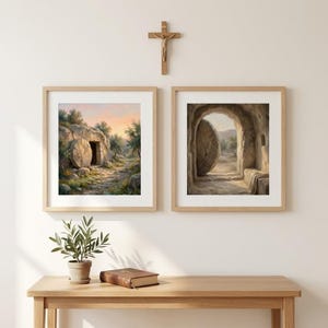 May include: Two framed art prints depicting a religious scene. One shows a tomb with an open door, the other a tomb with a large stone rolled away. A wooden cross hangs above the frames. A small plant and a book sit on a wooden table.