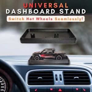 May include: A black rectangular universal dashboard stand with two small upright clips for securing a toy vehicle. The stand is shown empty and also holding a black toy pickup truck with red and white side graphics. Text reads UNIVERSAL DASHBOARD STAND.