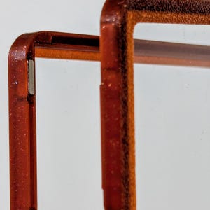 May include: Close-up of a phone case frame with a glittery, reddish-brown finish. The frame is designed with a clear center and features the text "Super strong N52 magnets". The frame has a magnetic strip.