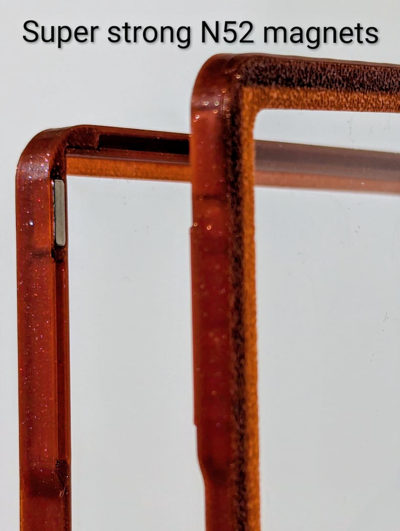 May include: Close-up of a phone case frame with a glittery, reddish-brown finish. The frame is designed with a clear center and features the text "Super strong N52 magnets". The frame has a magnetic strip.