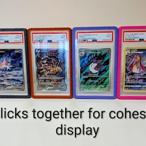 May include: Four graded Pok&eacute;mon trading cards in protective cases. The cases are black, orange, blue, and pink. The cards feature various Pok&eacute;mon characters and have text labels. The text at the bottom says "Clicks together for cohesive display."