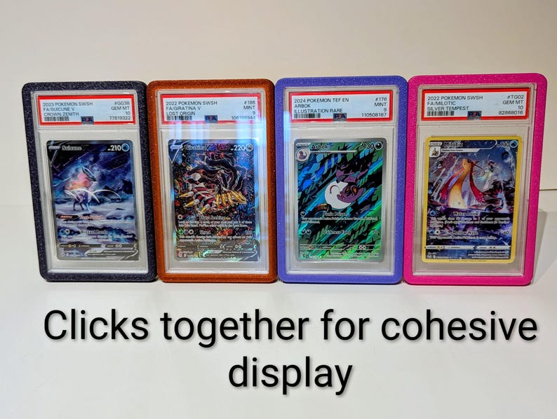 May include: Four graded Pok&eacute;mon trading cards in protective cases. The cases are black, orange, blue, and pink. The cards feature various Pok&eacute;mon characters and have text labels. The text at the bottom says "Clicks together for cohesive display."