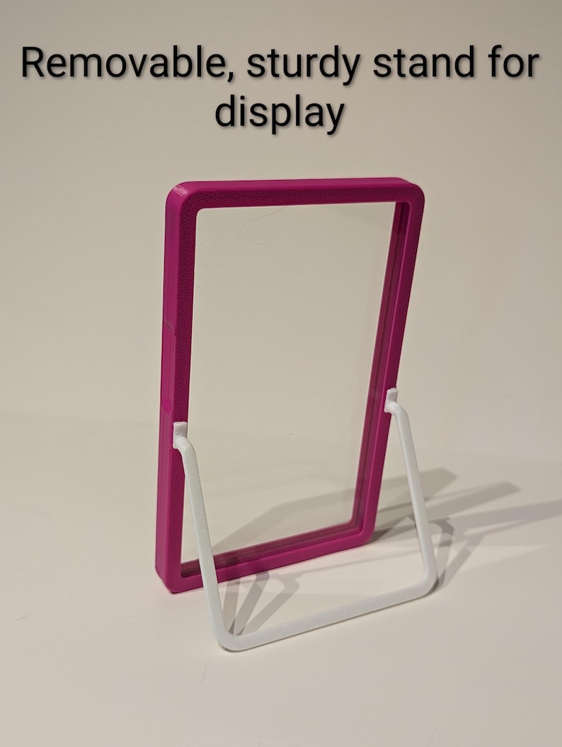 May include: A magenta display frame with a clear center, supported by a white, removable stand. The text "Removable, sturdy stand for display" is at the top. The frame is designed for showcasing items.