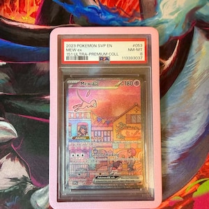 May include: A graded Pok&eacute;mon card featuring Mew ex, encased in a pink holder. The card displays colorful artwork of a town scene with the text "Genome Hacking" and "Restart". The holder has text indicating it's from the 2023 Pok&eacute;mon SVP EN 151 Ultra-Premium collection.