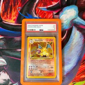 May include: A graded 1999 Pok&eacute;mon Game Charizard-Holo trading card in a protective case. The card features a yellow Charizard illustration with the text "120 HP" and "Fire Spin". The case has the text "1999 POKEMON GAME CHARIZARD-HOLO".