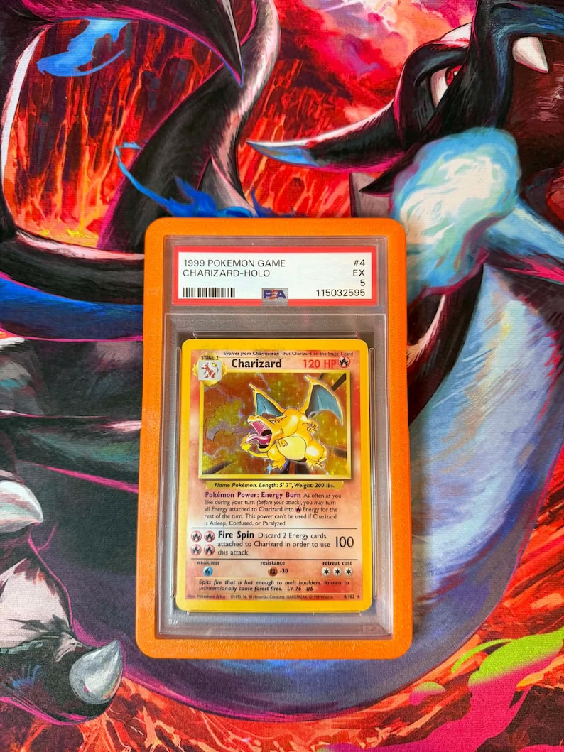 May include: A graded 1999 Pok&eacute;mon Game Charizard-Holo trading card in a protective case. The card features a yellow Charizard illustration with the text "120 HP" and "Fire Spin". The case has the text "1999 POKEMON GAME CHARIZARD-HOLO".