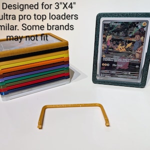以下が含まれることがあります： 3インチ x 4インチのカード用に設計された、カラフルなカードホルダーのスタック。緑色のホルダーに入ったカードの隣にあります。カードにはピカチュウのイラストが描かれています。金色のサポートピースも表示されています。画像には「Note: Designed for 3"X4" 25pt. ultra pro top loaders or similar. Some brands may not fit.」と書かれています。