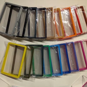 May include: A collection of colorful rectangular frames in various hues, including yellow, green, blue, and pink, are displayed. Each frame is individually packaged in clear plastic. The frames are arranged in two rows, showcasing a range of colors.