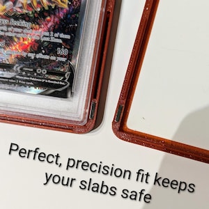 May include: A red-brown protective case for a trading card, with the card partially visible. The card has a colorful design with the number 160 visible. Text on the case reads "Perfect, precision fit keeps your slabs safe."