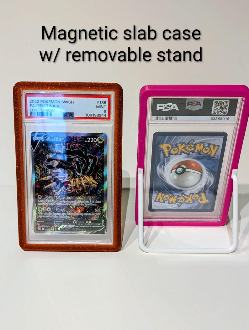 May include: Two magnetic slab cases with removable stands. One case is brown and the other is pink. The cases hold Pokemon trading cards. The text on the cases reads "Magnetic slab case w/ removable stand".