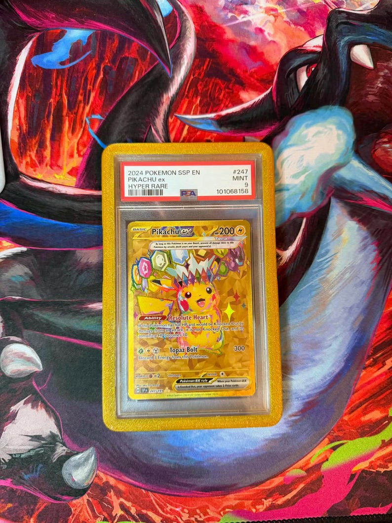 May include: A graded Pok&eacute;mon card featuring Pikachu ex from the 2024 SSP EN Hyper Rare set. The card is encased in a yellow holder and is graded as Mint 9. The card's artwork is predominantly yellow and gold, with the text "Pikachu ex" visible.