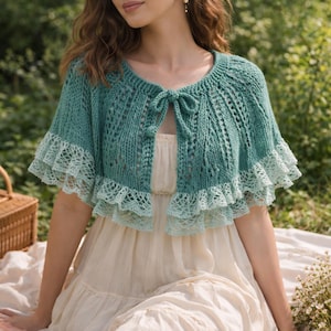 May include: A teal knitted shawl with a delicate lace trim and a bow closure. The shawl has a scalloped edge and is worn over a cream-colored dress. The design features openwork detailing and a soft, textured appearance.
